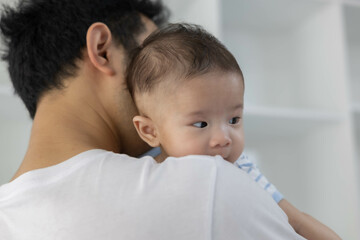 A man is holding a baby in his arms. The baby is wearing a blue and white striped shirt. The man is smiling at the baby, and the baby is looking up at him
