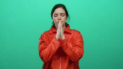 Woman in orange prison jumpsuit with handcuffs praying against green background captured in calm...