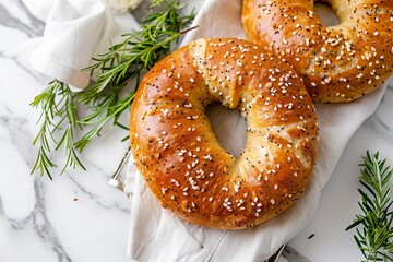 Two seeded bagels on a white cloth, placed on a marble surface with rosemary sprigs.