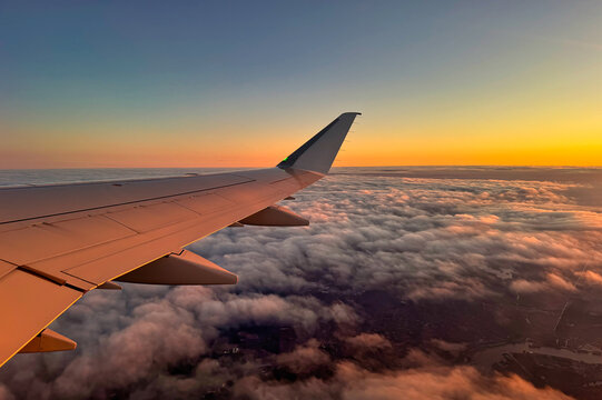 Wing of an airplane above clouds and land at sunset