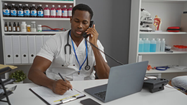 Handsome man in clinic speaking on phone while taking notes surrounded by medical equipment and supplies showcasing a professional healthcare setting.