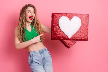 Cheerful young woman holding a glittery red gift box with a heart symbol in front of a vibrant pink...