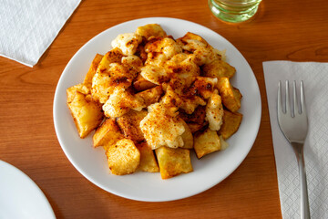 A plate of patatas bravas with aioli and spicy paprika served at the table, a popular Spanish tapa
