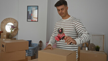 Young man packing boxes in a living room of a new home, preparing for a move with cardboard boxes...