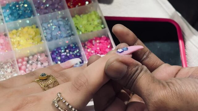 Title: Close-up of nail technician applying dark nail polish with precision, surrounded by colorful nail art accessories in professional salon nail extension preparation scene
