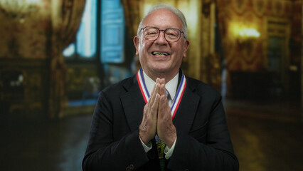 Senior man in business suit smiling with hands clasped wearing medal in museum setting indoor...
