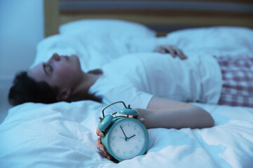 Frustrated young woman with alarm clock suffering from insomnia on bed indoors, selective focus