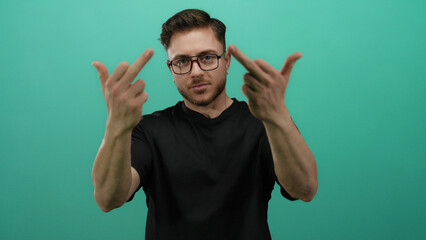 Fototapeta premium Young man with beard makes offensive gesture with middle fingers standing against isolated green background wearing black shirt and glasses