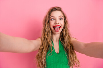 Playful young woman making a funny face while posing in a green outfit against a vibrant pink...