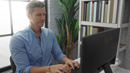 Young man working on computer in an office environment, reflecting concentration and focus,...