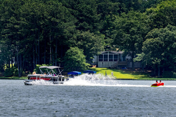 Pontoon boat pulling inflatable tube float raft on lake. Family on a pontoon party boat enjoying tubing on a summer day with their children.