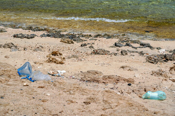 Plastic rubbish on a beach with sand rocks and coral remains, ocean shore pollution concept