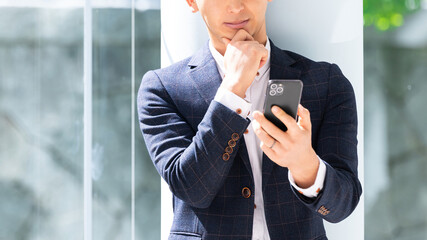 スマートフォンの画面を見て考える男性ビジネスマン