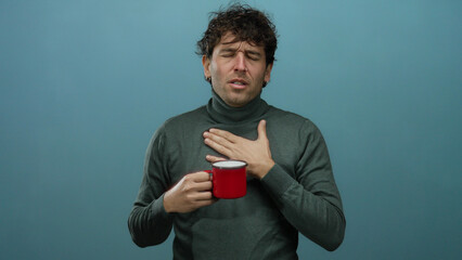 Hispanic man with a handsome appearance holding a red coffee cup against a blue background,...