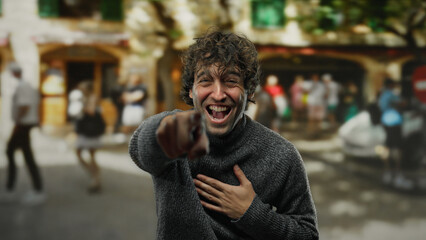Young man laughing and pointing in a bustling city street with blurred pedestrians in the background, capturing an energetic and vibrant urban outdoor atmosphere. © Krakenimages.com