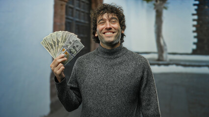 Hispanic man smiling while holding american dollars in an urban outdoor street setting, showcasing...