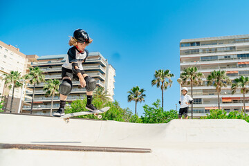 Young boy performing jump on skateboard in skatepark with palm trees