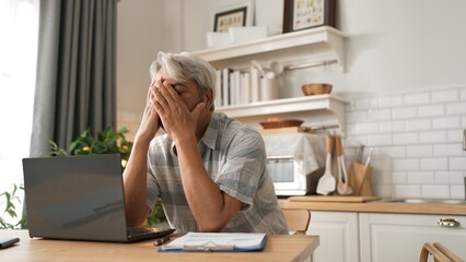 Stressed senior businessman holding head and thinking about solution while suffering from job problem or deceasing sales. Employee checking at computer while sitting at home. Remote working. Myrmidon.