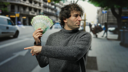 Hispanic man on city street holding russian rubles and pointing, depicting money and urban...
