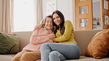 Obraz premium Warm moment of happy Caucasian family hugging each other. Beautiful girl embracing her mature mother while sitting together on sofa. Loving relatives happy about pleasant meeting at home. Relatives.