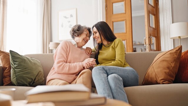 Warm moment of happy Caucasian family hugging each other. Beautiful girl embracing her mature mother while sitting together on sofa. Loving relatives happy about pleasant meeting at home. Relatives.