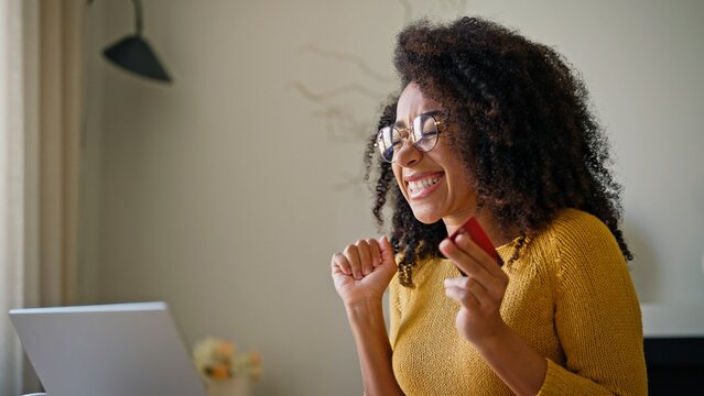 Pretty African American girl happy about successfully purchasing something on Internet. Satisfied woman holding credit card. Completing data for website on laptop. Widely smiling after buying.