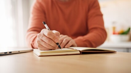 Close view of man's hands writing on paper with black pen. Making notes in notebook. Bright room....