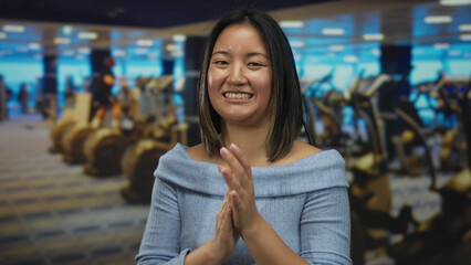 Woman clapping happily in a modern gym, with blue lighting reflecting on gym equipment, showcasing...