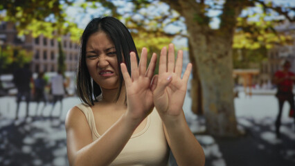 Woman expressing dislike outdoors in a sunny cityscape, surrounded by people and trees, capturing a candid moment in urban life.