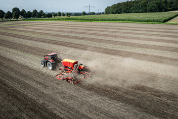 Traktor mit moderner Direkt - Sämaschine beim Drillen auf einem staubigen Feld, Luftbild.