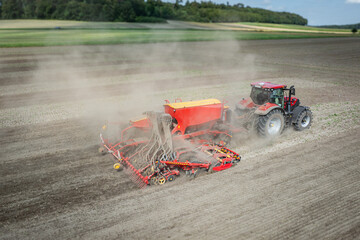 Traktor mit moderner Direkt - Sämaschine beim Drillen auf einem staubigen Feld, Luftbild.