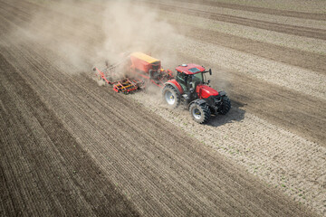 Traktor mit moderner Direkt - Sämaschine beim Drillen auf einem staubigen Feld, Luftbild.