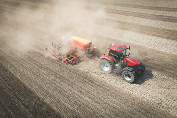 Traktor mit moderner Direkt - Sämaschine beim Drillen auf einem staubigen Feld, Luftbild.