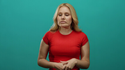 Woman in red shirt with blonde hair stands against blue background expressing confusion and...
