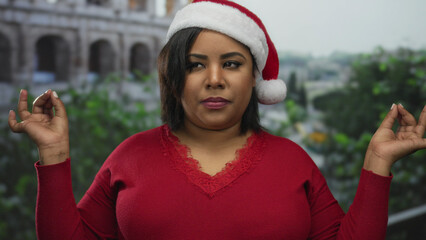 Latin woman in red sweater meditating with santa hat at the roman coliseum during christmas season.
