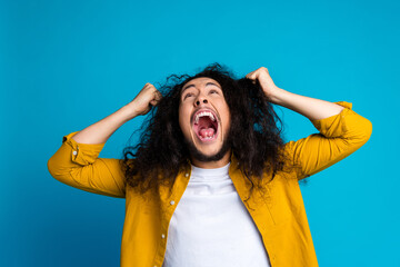 Excited young man with curly hair expressing emotions, pulling hair, wearing vibrant yellow shirt...