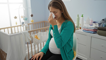 Pregnant woman sitting on a chair crying in a baby room with a cradle surrounded by baby clothes...