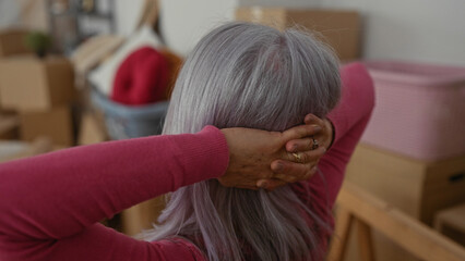 Senior woman with grey hair stretches in living room of new home surrounded by moving boxes and...