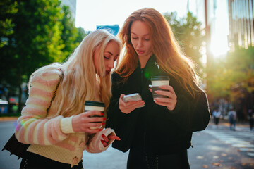 Two young women friends walking on summer sunny Seoul street, women looking on phone