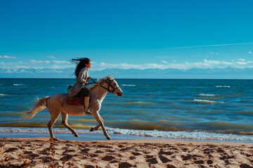 Young asian woman riding on horse on lake shore on summer day