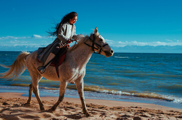 Young asian woman riding on horse on lake shore on summer day