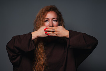 Young woman covers her mouth emotional portrait on gray background