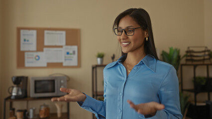 Smiling woman presenting in a cozy office setting with plants and a bulletin board in the...