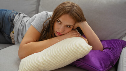 Woman relaxing indoors on a sofa, looking thoughtful and serene, in a cozy home setting with casual...