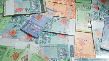 Malaysian banknotes showcasing various denominations of ringgit currency, including 50s, 10s, and 5s, spread out in a cluttered arrangement with detailed floral designs.