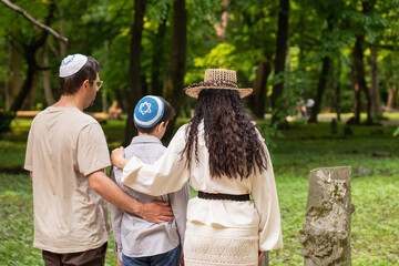 Mother, father and son jews at jewish cemetery pay respect to ancestors, jewish woman in wig and hat and long skirt, boy in kippah, girl in headscarf, jewish family
