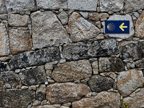 A blue for fatima and yellow Camino de Santiago sign with a scallop shell and arrow marks the pilgrimage route on a traditional, rustic stone wall background.