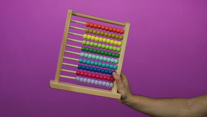 Caucasian man holding colorful abacus against vibrant pink background, emphasizing education and...