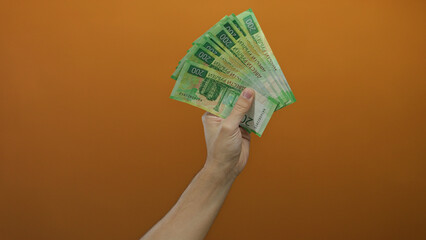 Caucasian man's hand holding russian rubles against an isolated orange wall background, depicting...