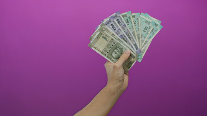 Caucasian man holding indian rupee banknotes in hand against a vibrant pink wall, showcasing...